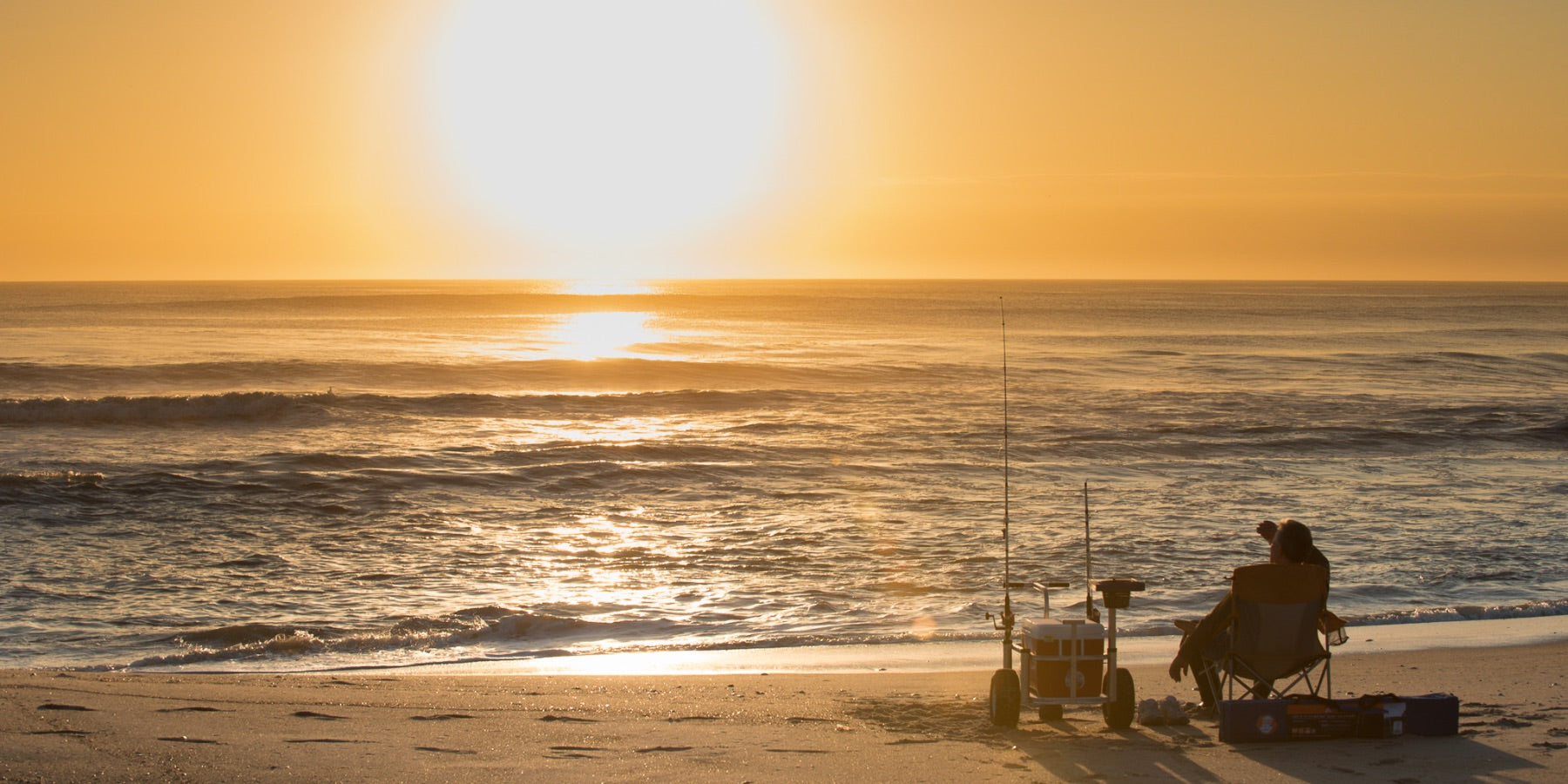 A fishermen watches the sunrise in Avon North Carolina while fishing on the beach. 